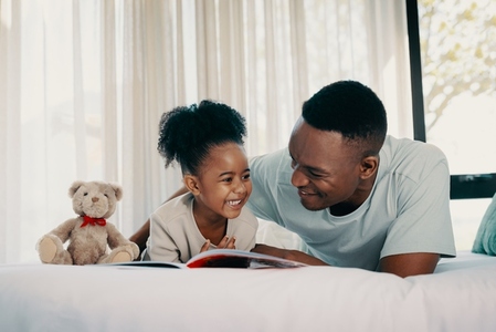 Happy child enjoying a story book with her dad