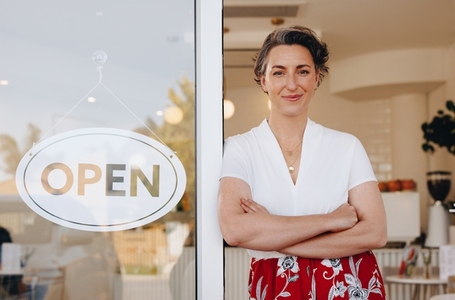 Mature small business owner standing at the entrance of her newly opened cafe
