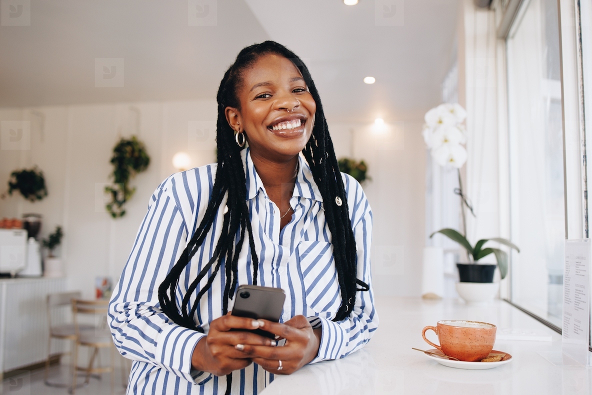 Portrait of a happy young businesswoman smiling at the camera while holding a smartphone in a cafe