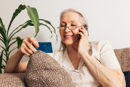 Aged woman holds a credit card and makes a call on mobile phone