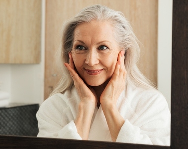 Portrait of a smiling mature woman with grey hair looking at a mirror in bathroom