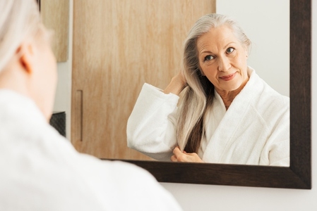 Portrait of an aged female with long grey hair looking at a bathroom mirror