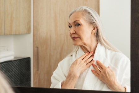 Aged woman in a bathrobe looking at the skin on her neck