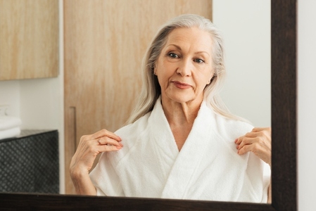 Senior woman adjusting her bathrobe in front of a mirror