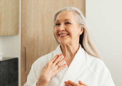 Happy senior woman looking at her reflection in the mirror in morning in the bathroom