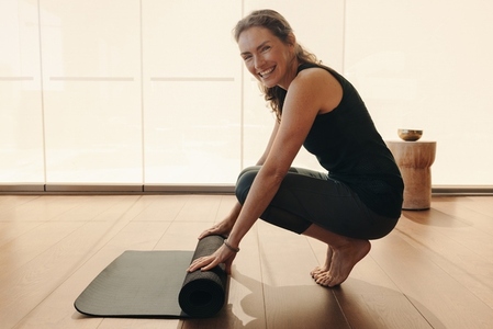 Healthy senior woman rolling up an exercise mat at home