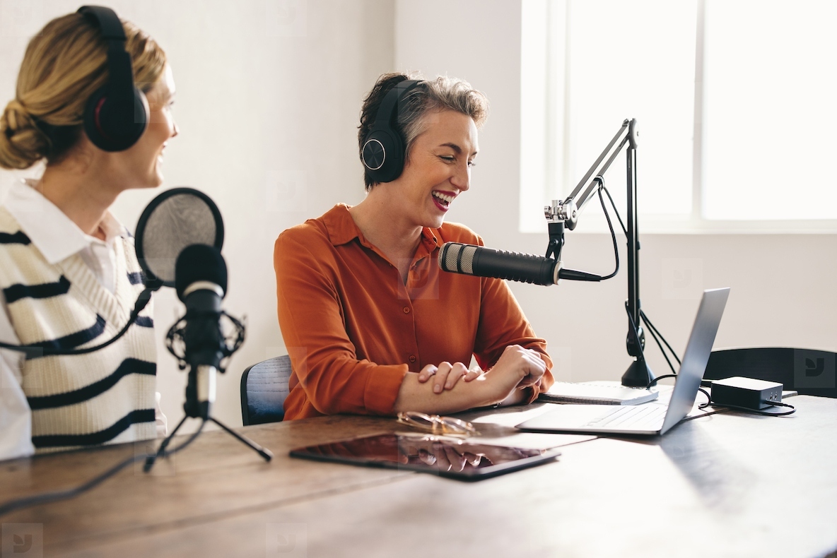 Happy female podcasters co-hosting a show in a home studio
