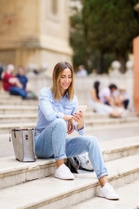 Glad woman with smartphone sitting on steps