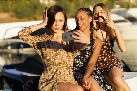 Positive multiracial women taking selfie in port