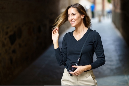 Confident lady with camera smiling and touching hair on street