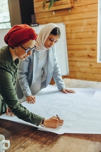 Two Muslim designers working on blueprint drawings in an office