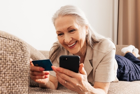 Close up on a happy aged woman with grey hair making a purchase by smartphone and a credit card