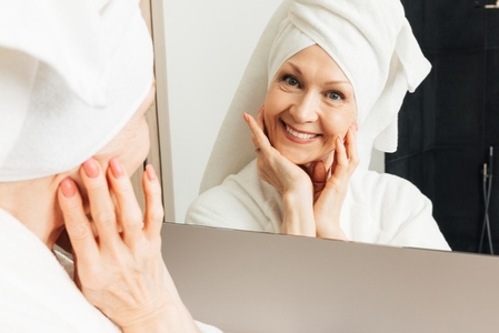 Cheerful senior woman with towel on head looking at camera