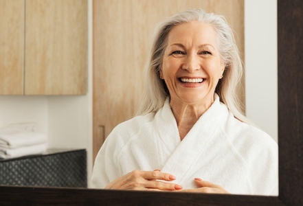 Laughing aged woman in a bathrobe in front of a mirror in the bathroom