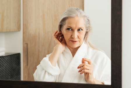 Aged female adjusting her grey hair in the bathroom