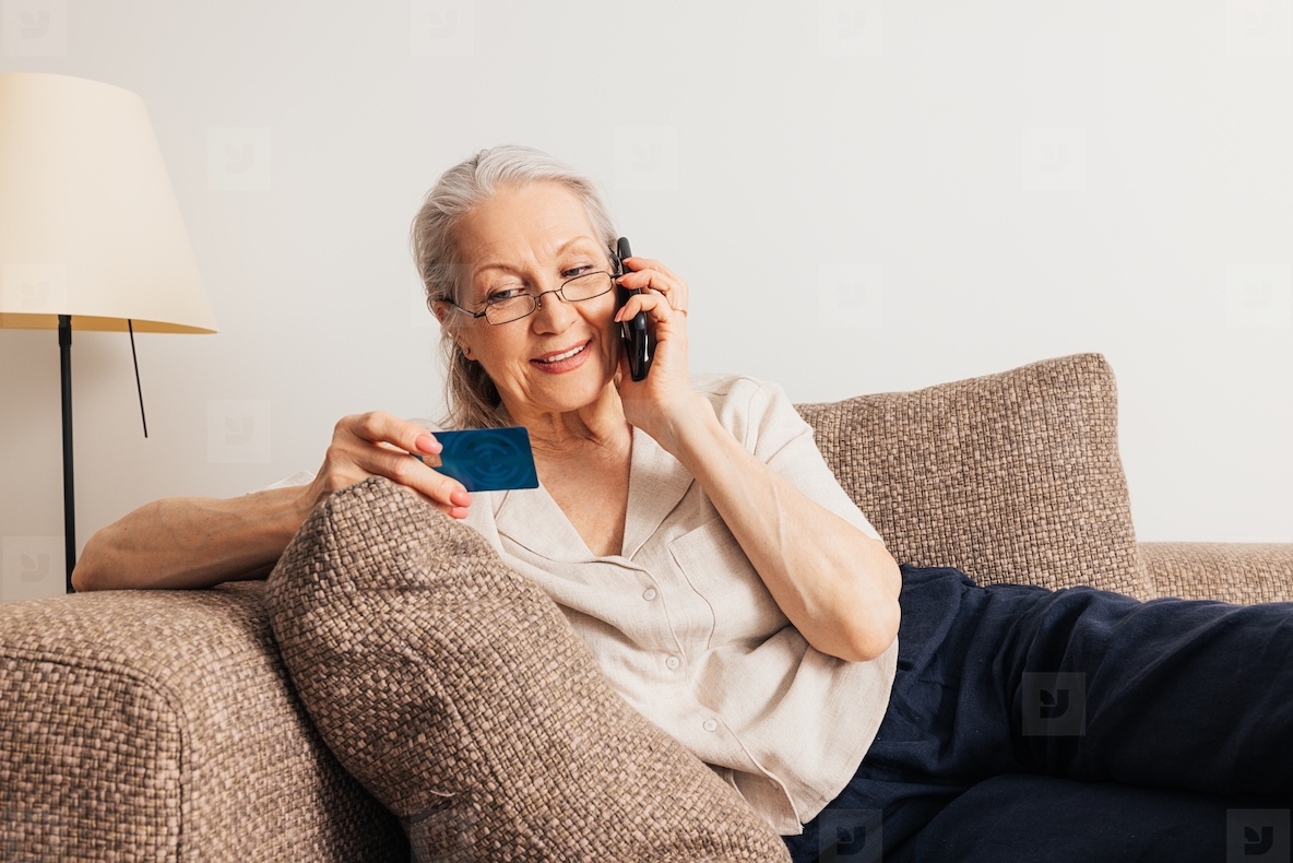 Aged woman making a call and holding a credit card. Senior female making an online order