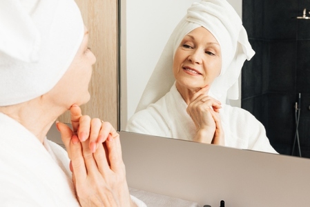 Aged woman admire her face in bathroom
