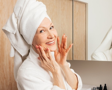 Smiling senior woman with a towel on her head massaging her face and looking at camera