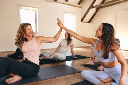 Two women high fiving each other in a yoga class