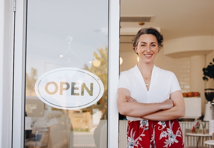 Successful cafe owner smiling while standing at the doorway of her newly opened restaurant