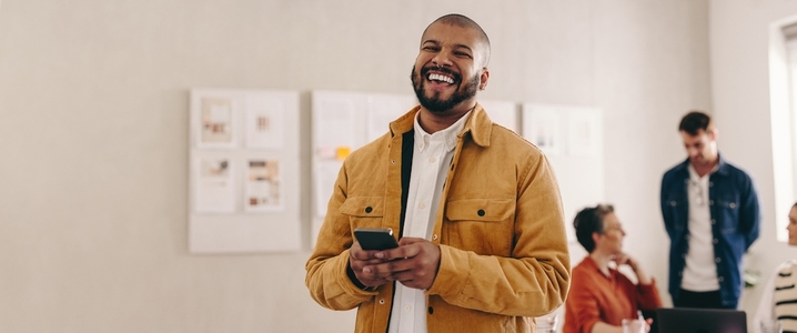 Modern businessman smiling at the camera while holding a smartphone
