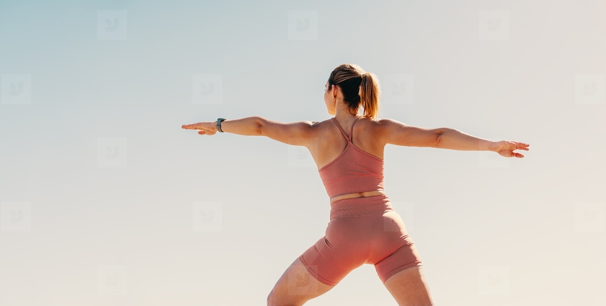 Woman practicing warrior pose outdoors in sportswear for physical fitness, wellbeing and health
