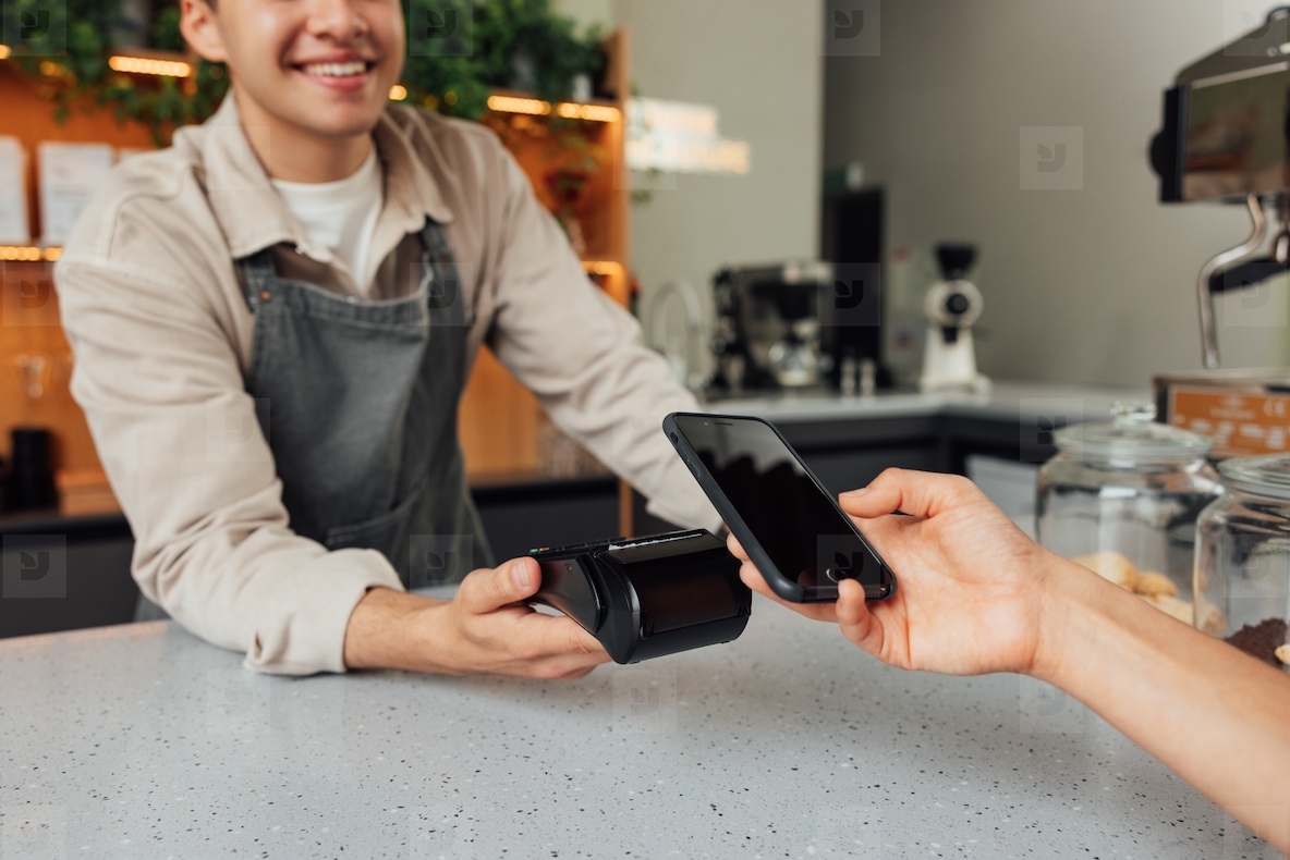 Unrecognizable cafe owner holding card machine at the counter while customer making payment by smartphone
