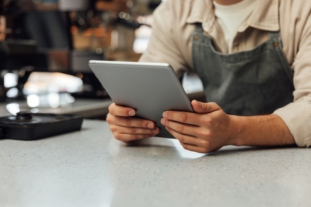 Close up of hands holding a digital tablet  Unrecognizable bartender in an apron holding a portable computer at the counter