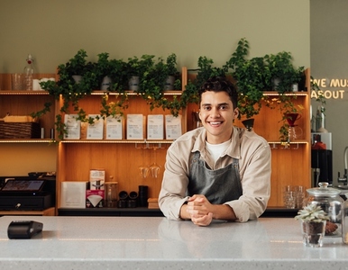 Smiling coffee shop owner in apron leaning a counter  Middle eastern bartender looking at camera
