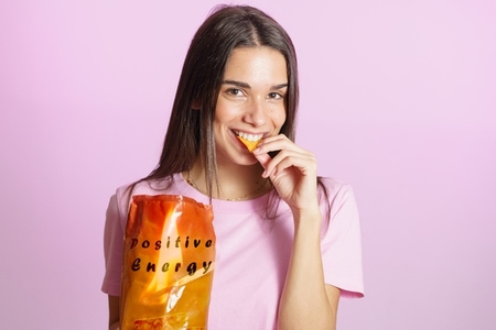 Woman eating tasty crisps pink background