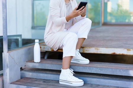 Unrecognizable woman using smartphone sitting on steps near her office  Famela taken a coffee break