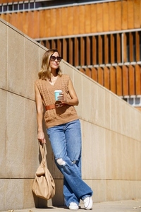 Stylish woman with coffee leaning on wall