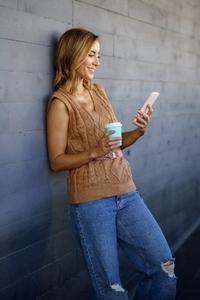 Cheerful female with smartphone and coffee leaning on wall