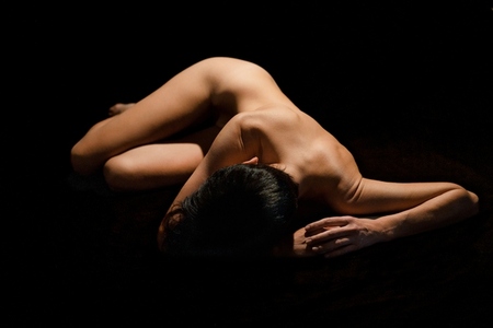 Unrecognizable woman with naked body lying in black studio