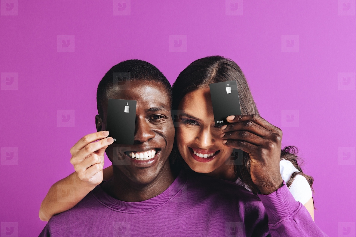 Happy couple holding black credit cards in a studio, recommending electronic banking