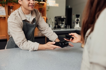 Cropped of a male bartender holding a card machine while customer paying by mobile phone
