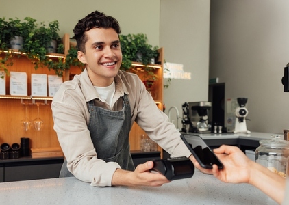 Smiling male barista holding pos terminal looking at the customer  Bartender receive contactless payment