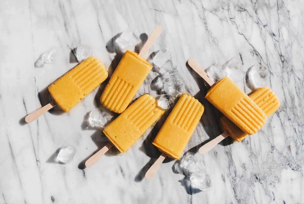 Flat-lay of homemade mango smoothie vegan popsicles over marble background