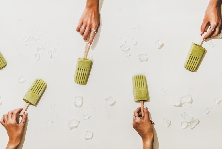 Womens hands with green matcha coconut popsicles over white background