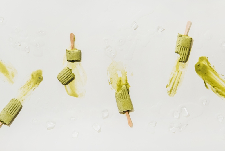 Flat-lay of melting green matcha coconut popsicles over white table