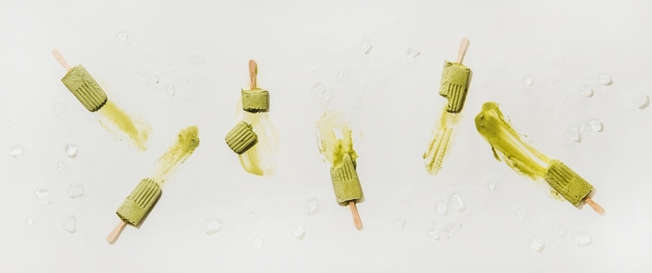 Flat lay of melting green matcha coconut popsicles over white table