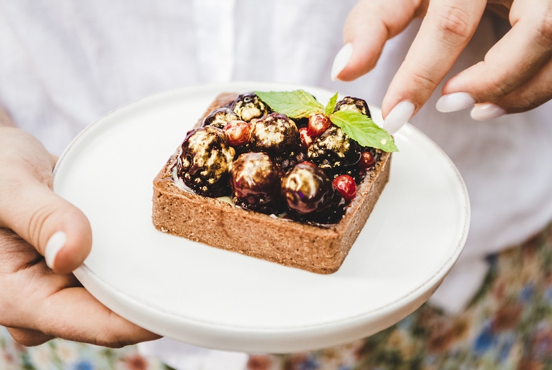 Woman taking cocoa tartalette with fresh berries from white plate