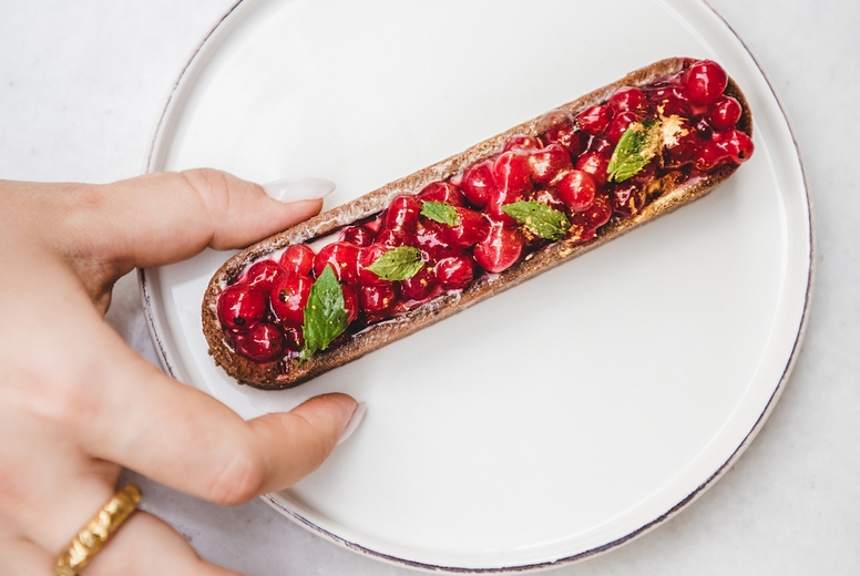 Womans hand taking tart with seasonal fresh red currant berries