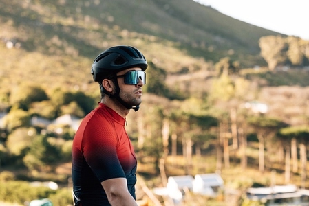 Portrait of male cyclist in helmet and glasses looking away while standing against a mountain