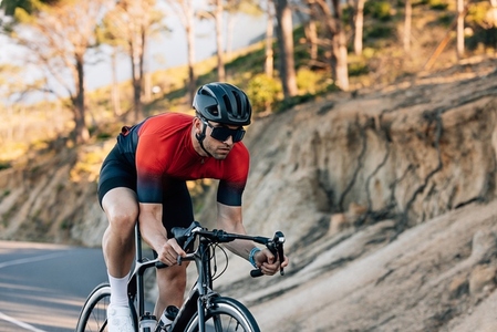 Professional cyclist going down a hill  Athlete in helmet and glasses riding road bike outdoors
