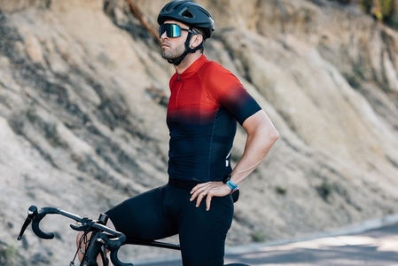 Male cyclist in sportswear standing on a road with bicycle relaxing after ride