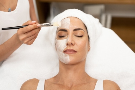 Aesthetics applying a mask to the face of a Middle aged woman in modern wellness center
