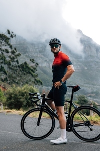 Full length of male cyclist relaxing during training  Professional cyclist standing against a mountain and looking away