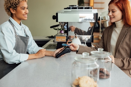 Client paying by card at a coffee shop  Smiling barista holding pos terminal while customer paying