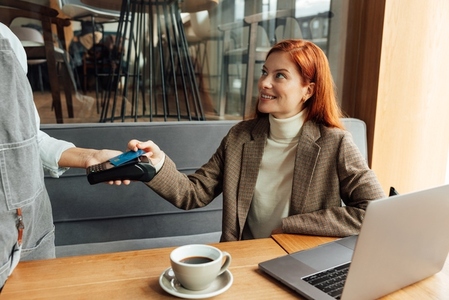 Smiling businesswoman with ginger hair paying by card in coffee shop